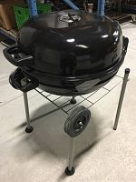 Black metal portable charcoal BBQ grill with dome lid on wire stand with two wheels on concrete floor.