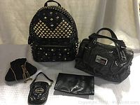 Photo showing all five purses together: MCM studded backpack, Guess handbag, BabyPhat small purse, Goldco formal purse, and black leather-like purse.