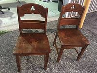 Two solid oak vintage church chairs with carved backrest and original finish, placed outdoors on asphalt.