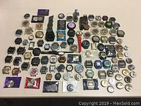 Photo showing an extensive assortment of watch parts including watch cases, watch faces, watch bands, and individual watch backs spread out on a table.