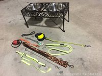 Full lot overview showing the cast iron elevated food station with two stainless steel bowls and several dog collars and leashes arranged on the floor.