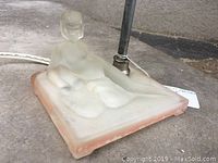 Close-up photo of the frosted glass female nude figure integrated in the square base of the lamp, showing details and condition.
