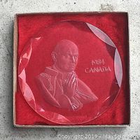 Image of the round engraved plastic plaque featuring St. Pope John Paul II in prayer, with text '1984 CANADA', set on red velvet inside box.