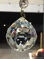 Close-up of a clear faceted crystal chandelier ball hanging on a metal hook, showing geometric cuts that reflect light.