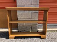 Wood bookcase front view showing two shelves and smooth wood finish, placed outside against a gray wall.