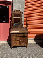 Full front view of the antique solid wood dry sink washstand showing the attached mirror with carved detail, drawers, cupboard, and towel bar on the right side.