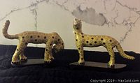 Image of two leopard figurines on wooden stands, showing side views and posture differences.