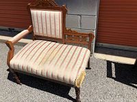 View of vintage gossip bench showing carved wooden frame and striped upholstery with damaged corner on the seat