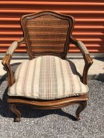 Front view of the chair with a striped cushion on the cane seat, showing wooden frame and cane backrest, upholstered armrests.