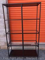 Front view of a black metal frame shelving unit with 3 glass shelves and wood top/bottom shelves.
