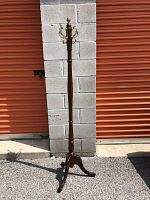 Full length view of wooden Bombay coat rack standing upright on asphalt in front of block wall and orange roll-up doors.