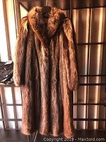 Front view of full-length raccoon fur coat hanging against shelving