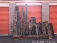 23 assorted vintage barn wood boards leaning against orange storage unit doors, showing varied lengths and widths with rustic, weathered surfaces.