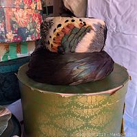 Side view of the feathered vintage hat showing its intricate feather details and a green decorative hat box beneath it.