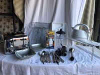 Full view of toaster, kettle, blender/mixer, food chopper, cutlery baskets, cutlery assortment and silver bowls on white cloth background.