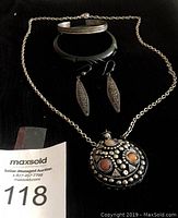 Entire set of jewelry displayed on black background, featuring silver pendant necklace with stopper, silver bangle bracelet, green bracelet, and silver drop earrings.
