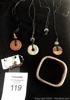 Three pendant necklaces, one silver bracelet, and hoop earrings on black background