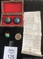 Pair of iron Baoding balls with colored dragon motifs in decorative box, accompanied by an information leaflet about Baoding balls