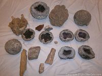 Full view of collection on white cloth showing several amethyst geode halves with purple crystalline interiors, desert rose mineral, spherical rocks, petrified wood, and other minerals.