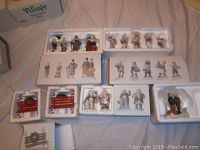 Overview of boxed and loose Studio 56 holiday figurine sets in styrofoam packaging including elves, Santa & Mrs Claus, shoppers, man and dog, and candy cane benches.