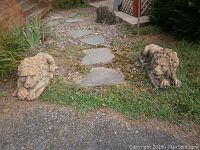 Two stone lion statues side by side on the edge of a gravel path, showing overall set