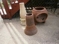 Photo of the outdoor clay chiminea pieces with round fire chamber and cylindrical chimney, plus the stone pedestal in background
