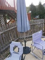 Overall lot showing the two rocking chairs, lounger, and patio umbrella on outdoor concrete surface with wooden fence background.