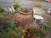 Full front view of the large pottery planter situated outdoors next to a metal garden chair and flowers, showing overall size and environment.