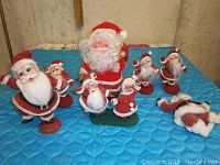 Overview of seven Santa Claus figurines arranged on blue quilted surface