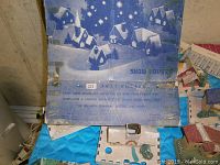Photo showing a snow house cardboard box with blue and white winter village illustration and usage instructions for electrical lighting of paper houses.