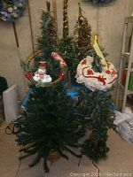 Photo showing two artificial Christmas trees, one with snowman ornament and one smaller with white hat decoration on top.