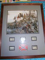 Framed Mort Künstler print showing a detailed Civil War battle scene with soldiers and horses. Below the image are five postage stamps and a Confederate flag patch mounted on a gray mat within the wood frame.