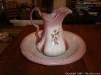 Antique ironstone pitcher and basin set displayed on a wooden surface, showing front view with floral decoration and embossed details.