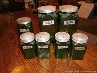 Photo showing all 7 green glass jars with labels arranged on a wooden surface.