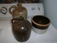 Two stoneware jugs and one bowl placed on a white surface against a washer background.