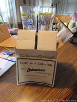 Photo showing four Galaxy Quest collectible glasses with colorful character designs and logos, with the Certificate of Authenticity resting on the table in front of a cardboard box.