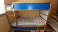 Fully assembled IKEA KURA bunk bed in a child's bedroom, showing the blue sides and wooden frame with mattress on lower bunk.