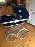 Full side view of large vintage blue Perego pram with metal frame and large wheels on hardwood floor.