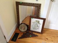 Photo showing all items together including the large mirror, two framed prints, and wooden decorative piece on floor near wall and door.