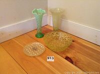 Two green glass vases, green glass bowl, and two clear textured plates on wooden floor