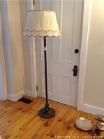 Full view of vintage floor lamp with fabric outer shade showing damage, standing next to a door on wood floor.