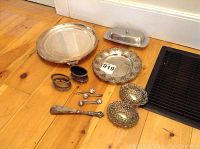 Full lot overview of all silver and silver-plated pieces on floor, including shoe horn, dishes, spoons, and holders.