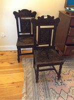 Pair of dark carved wooden dining chairs with floral and scroll detailing, showing overall condition.