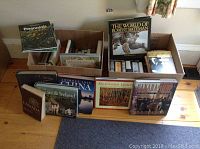 Two open boxes filled with various books on topics including Robert Bateman's wildlife works, Group of Seven art, travel guides, Canada, and novels by Henning Mankell.