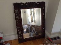 Full view of rectangular mirror leaning on wall showing carved wood frame and reflection.