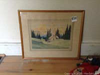 Framed watercolour landscape painting showing overall view with wooden frame and matte, placed on wooden floor.