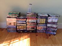 Wide view of four stacks on wood floor against wall: three stacks of DVDs and one of VHS box sets