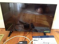 Front view of the 28-inch Insignia LED TV with a power cord, remote, and manual on wooden floor.