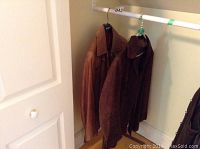 Two jackets hanging on a closet rod, one darker suede, one lighter leather