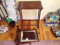 Photo of a wooden table with decorative inlay top, broken and wobbly base, with detached mirror placed underneath on wooden floor